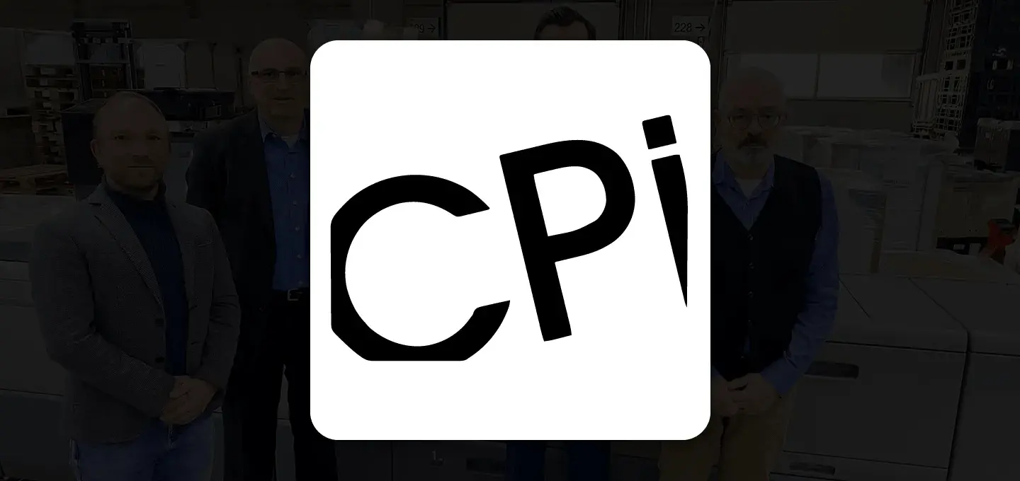 A group of people standing in an industrial warehouse, smiling, with stacks of goods and machinery in the background. A white "CPi" logo overlays on the right.