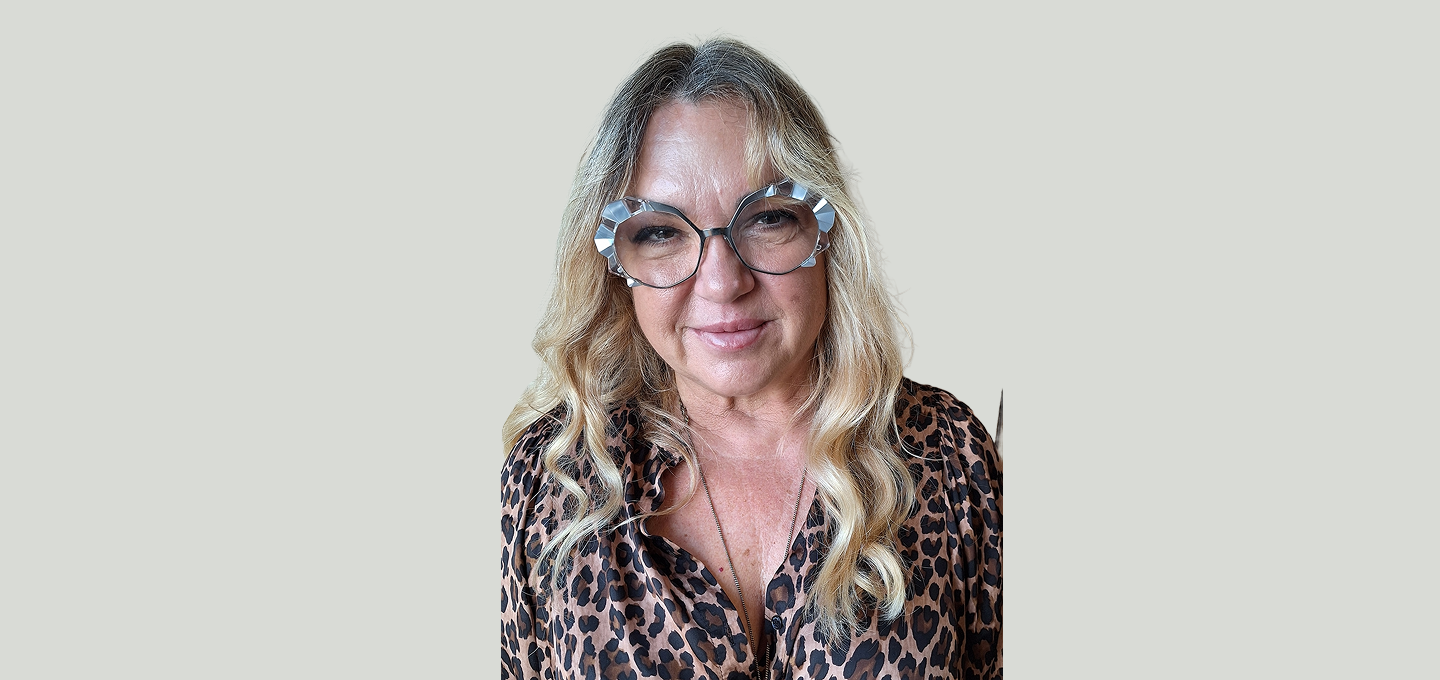 Person wearing a leopard‑print blouse with long wavy blonde hair, photographed indoors against a neutral background