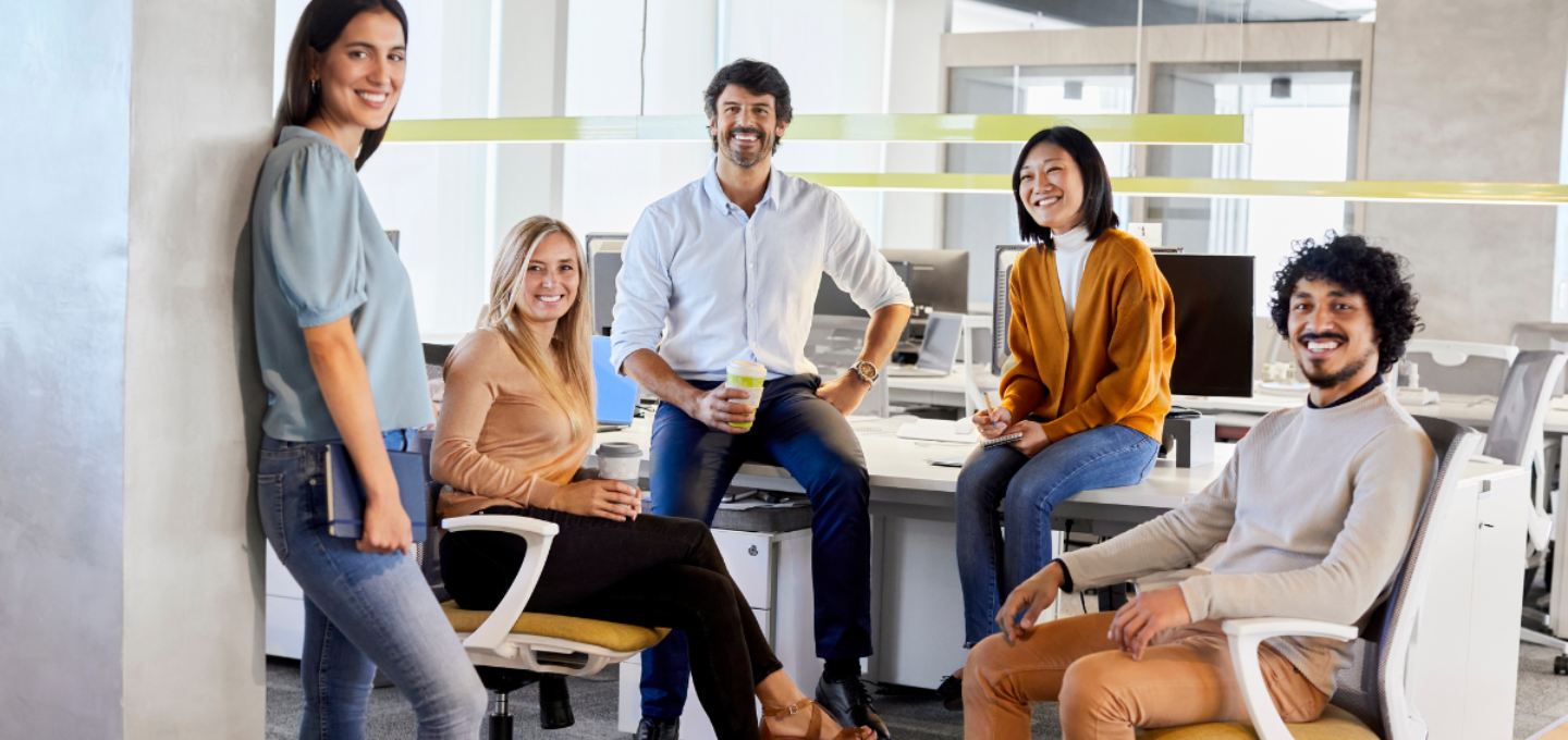Workplace Experience as a Service - Persone in ufficio sedute attorno a una scrivania e sorridenti